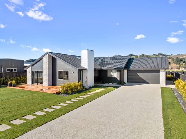 Modern single-story house with dark siding, a white chimney, metal roof, and concrete driveway.